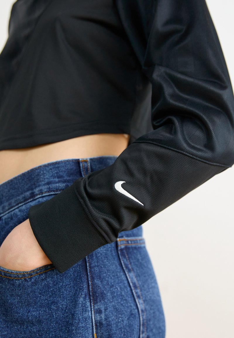 Top lungo nero a maniche corte con finitura texturizzata e logo Nike bianco sul polsino, abbinato a jeans denim blu a vita alta.