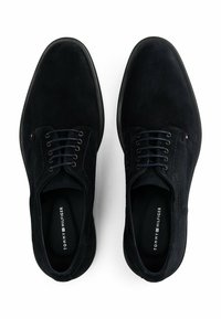 Donker marineblauwe suède schoenen met een gladde textuur, voorzien van zes veterogen, blauwe stiksels en rubberen zolen. Merkennaam zichtbaar aan de binnenkant.