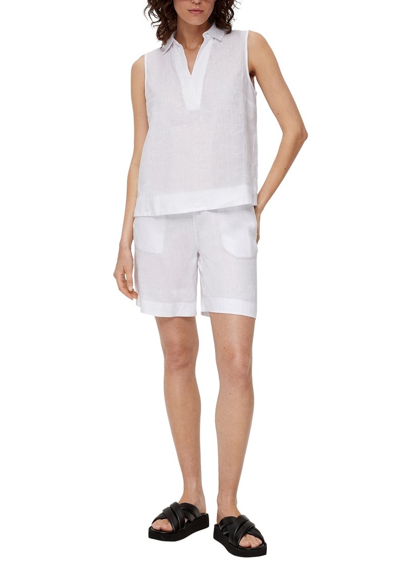 Femme portant un haut blanc sans manches à col et un short blanc assorti avec des poches avant, assortis à des sandales à plateforme noires.