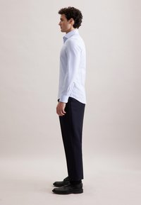 Lichtblauw gestreepte overhemd met lange mouwen, met een hellende zoom, gecombineerd met zwarte broek en zwarte nette schoenen. Netjes en goed passend ontwerp.