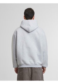 Sudadera con capucha de color gris claro, de corte relajado, con tejido texturizado, puños y dobladillo de canalé. Presenta una gran capucha en la parte trasera y hombros caídos.