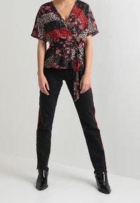 Wrap bluse i sort med røde blomster- og dyreprint mønstre, parret med slanke sorte jeans med røde sidelækker og sorte ankelstøvler.
