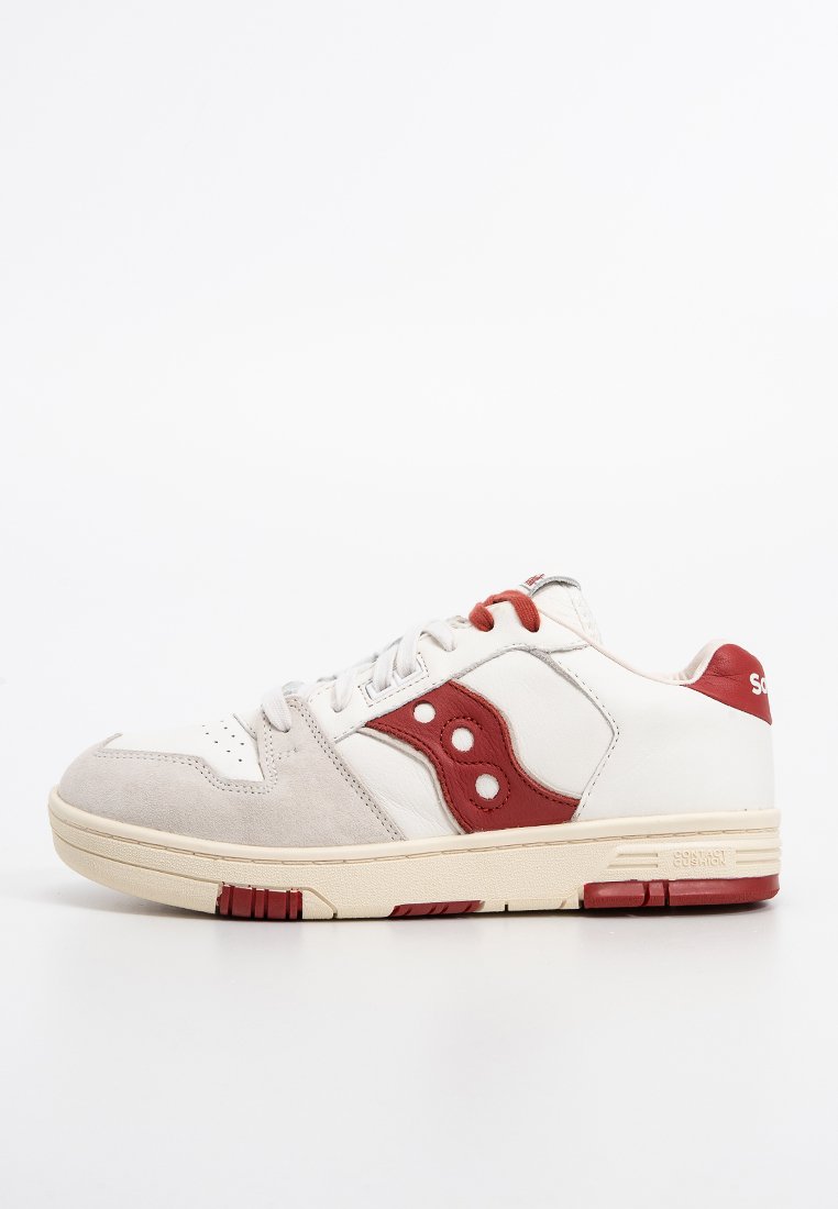 Sneaker bianca con accenti rossi, materiali in suede e pelle, punta rotonda, suola piatta, logo prominente di lato, dettagli testurizzati sulla linguetta.