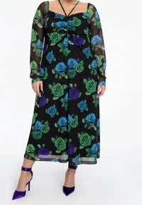 Robe noire à motifs floraux avec des roses vertes, bleues et violettes ; manches longues en voile transparent ; corsage ajusté ; longueur cheville ; accompagnée de talons violets.