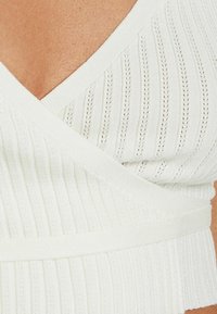 Vit ribbad stickad topp med djup V-ringning och inslagningdesign, i texturerat tyg och med åtsittande midja.