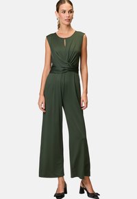 Green jumpsuit with a fitted bodice, wide-leg trousers, and a keyhole neckline. Made of soft fabric with a twisted detail at the waist.