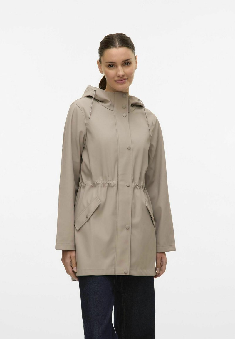 Giacca impermeabile beige con cappuccio, vita regolabile con coulisse, bottoni a pressione e due tasche laterali. Tessuto liscio e vestibilità rilassata.