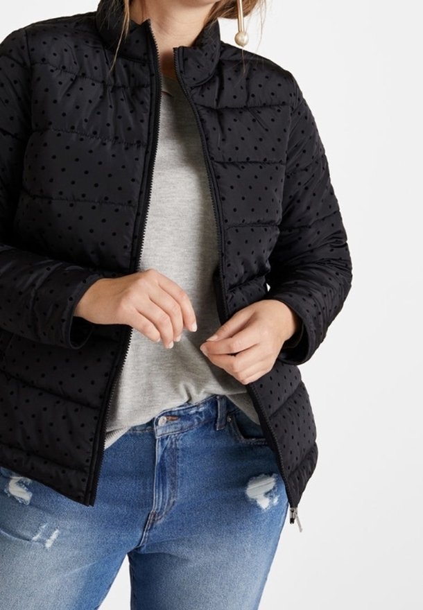 Black puffer jacket with polka dot pattern, zip front, standing collar, and textured fabric. Worn over a gray shirt and distressed jeans.