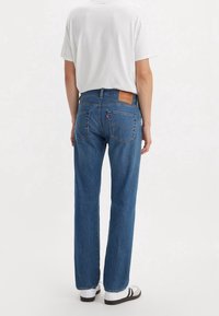 Blå denimjeans med rak bendesign, som har bakfickor och en brun läderlapp på midjebandet. Bärs med en vit t-shirt.