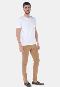 T-shirt bianca in cotone, pantaloni khaki e scarpe scure con accenti chiari. Design semplice, maniche corte e un piccolo logo sulla maglietta.