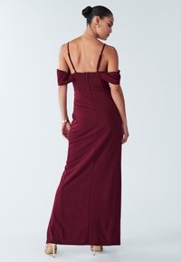 Bordové šaty bez ramínek s přiléhavým korzetem, zapínání na zip vzadu a dlouhou, volnou sukní. Hladký povrch látky.