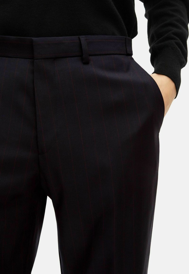 Dark pinstriped trousers made of smooth fabric, featuring a straight cut, side pockets, and a flat front waistband with belt loops.