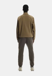 Beige Jacke mit entspannter Passform, kombiniert mit dunkelgrauen, schmal zulaufenden Hosen. Das Outfit hat eine glatte Textur und elastische Bündchen, getragen mit weißen Sneakers.