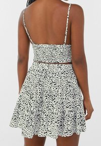 Schwarzes und weißes Blumenmuster-Kleid mit verstellbaren dünnen Trägern, gerafftem Oberteil und ausgestelltem Rock. Leichter Stoff mit strukturiertem Aussehen.