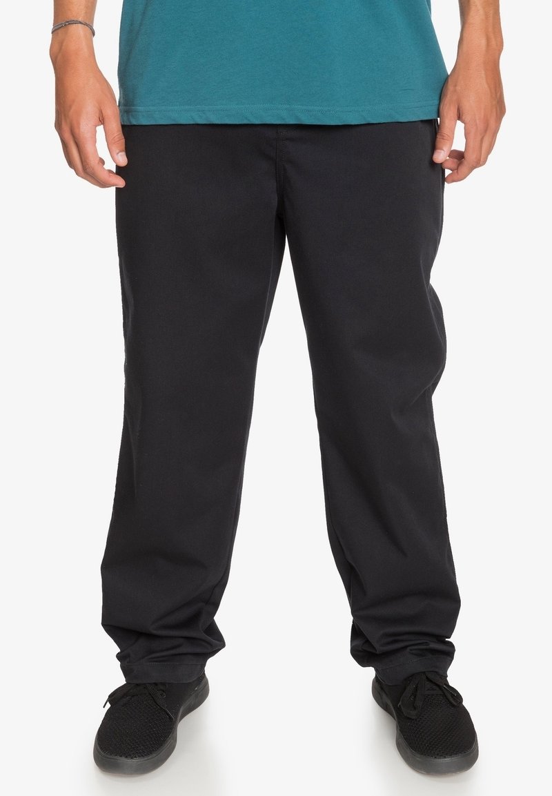 Černé kalhoty s rovnými nohavicemi vyrobené z odolné látky, s hladkou texturou a jemnými švy. Nošeny s černými botami.