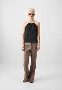 Melns haltera tipa tops ar savāktu kakla izgriezumu, kombinēts ar bēšām, vidukli piesedzošām plaša stila biksēm. Modelis valkā gaišas saulesbrilles.