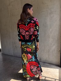 Maxi sukňa s multikolórovým kvetinovým vzorom na čiernom podklade; skombinovaná s živým sveterom s červenými, tyrkysovými a ružovými vzormi.