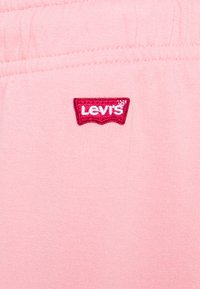 Pink sweatshirt fabric with visible stitching; features a red embroidered Levi's logo on the front. Soft texture and casual design.