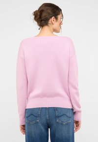 Rosa Strickpullover mit lässigem Schnitt, weitem Ausschnitt und gerippten Bündchen, kombiniert mit blauen hochgeschnittenen Jeans mit einem auffälligen Taschendesign.