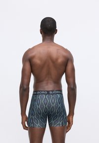 Bakgrunnsbildet viser en skjorteløs mann iført mønstrede Björn Borg boxershorts mot en enkel hvit bakgrunn.