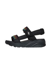 Sandalias negras con correas de tela que presentan acentos verticales coloridos. Suela gruesa y texturizada con un diseño curvado y correa ajustable en el talón.