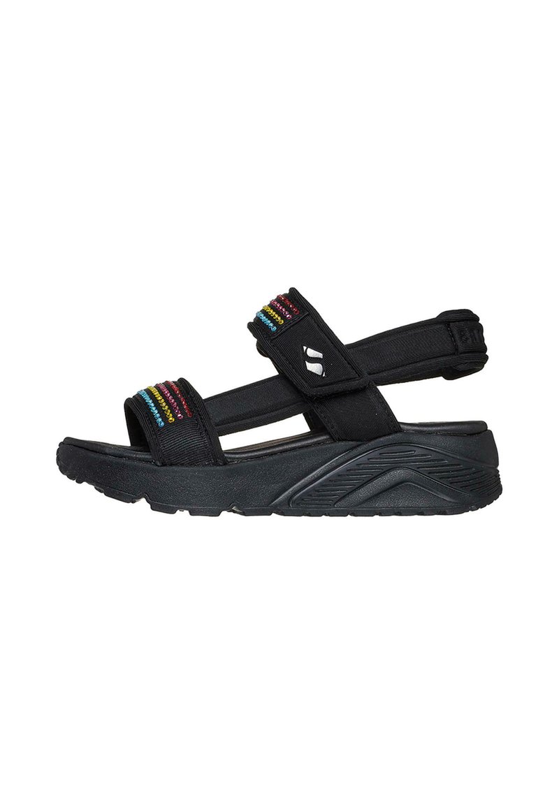 Sandalias negras con correas de tela que presentan acentos verticales coloridos. Suela gruesa y texturizada con un diseño curvado y correa ajustable en el talón.