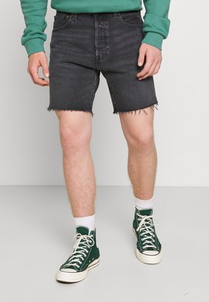 Homme portant un short en denim noir avec des ourlets effilochés, des baskets montantes vertes, des chaussettes blanches et un sweat-shirt vert visible à la taille et aux manches.