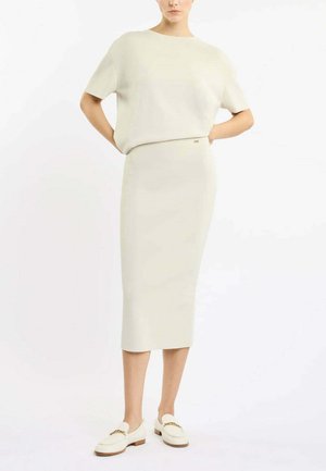 Ensemble en tricot deux pièces en tissu doux blanc cassé, comprenant un haut ample à manches courtes et une jupe crayon fitted mi-longue. Éclairé par un branding subtil.