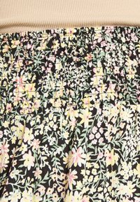 Tecido com padrão floral, apresentando pequenas flores em tons pastel sobre um fundo preto, com uma cintura franzida em textura canelada bege.
