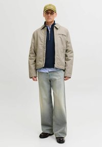 Beeži jakk, millel on lukuga ees, navy sinise sviitri peal, sinine kraega särk ja laiad helesinised teksad. Oliivroheline müts ja mustad jalanõud lõpetavad välimuse.