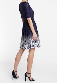 Námorní dress s krátkými rukávy, s gradientem bílých puntíků na lemu. Skládaná sukně, hladký materiál. Nosit s černými podpatky.