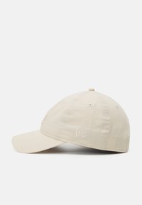 Beige színű baseball sapka, amely szövetből készült, ívelt napellenzővel, hímzett logóval az elején és szellőzőlyukakkal a korona részén.