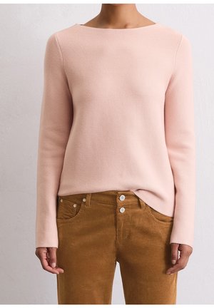 Persona vistiendo una blusa de punto de manga larga de color rosa claro metida en unos pantalones de pana marrones de cintura alta con doble botón.