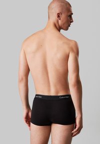 Black cotton trunk with a soft waistband featuring "Calvin Klein" branding. Smooth texture and fitted design. Standard mid-rise cut.