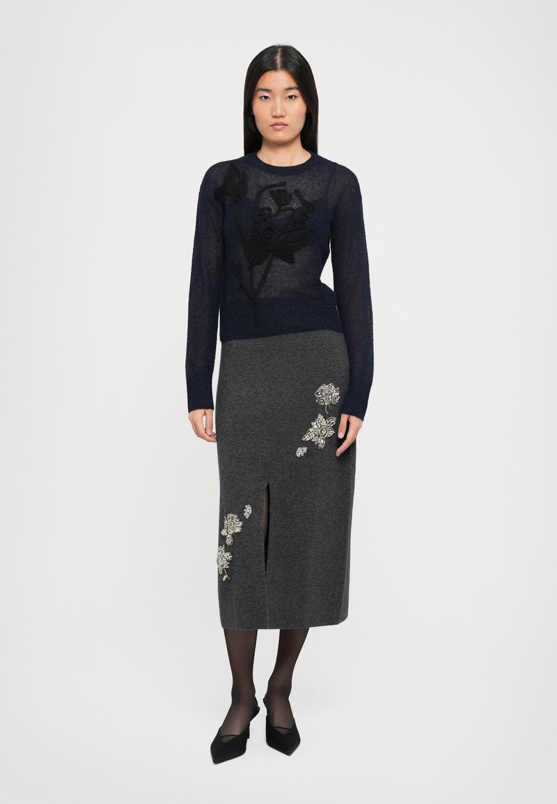 Maglione lungo a maniche sheer color navy con ricami floreali neri, abbinato a una gonna a tubino grigia in maglia con applicazioni floreali e uno spacco.