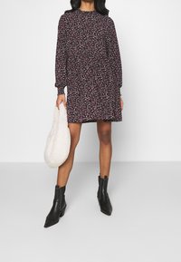 Kwiatowa sukienka z wysokim dekoltem, długimi rękawami i dopasowaną talią. Ciemnofioletowe tło z małymi różowymi i białymi kwiatami. Czarne botki za kostkę.