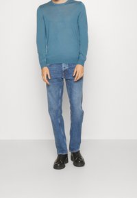 Suéter de punto azul claro de manga larga, combinado con pantalones vaqueros azules y zapatos negros con cordones. Vestimenta simple y casual.