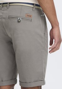Shorts en coton gris avec des revers, dotés d'une poche arrière avec fermeture à bouton et d'un label en cuir. Accentué par une ceinture rayée.