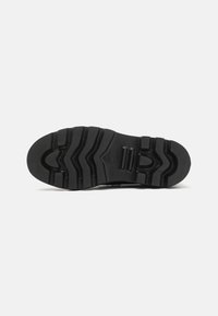 Suela de zapato de goma negra que presenta un patrón de banda de rodadura con estrías y surcos para mayor tracción; está hecha de un material suave y duradero.