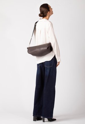 Borsa a tracolla in pelle marrone dalla forma arrotondata, caratterizzata da dettagli in metallo argentato e una superficie testurizzata, indossata a tracolla su sfondo chiaro.