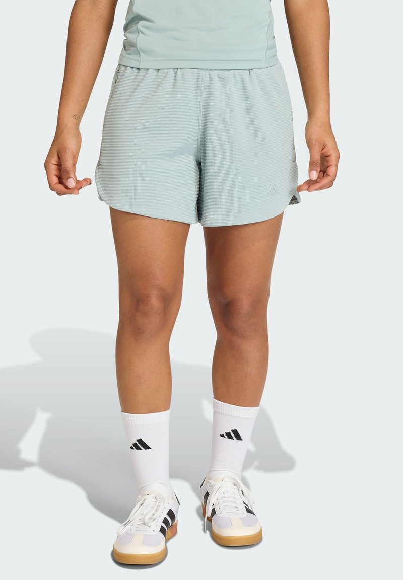 Lichtblauwe sportshorts met een gestructureerde stof, elastische tailleband en zijopeningen. Gecombineerd met witte sokken en meerkleurige sneakers.