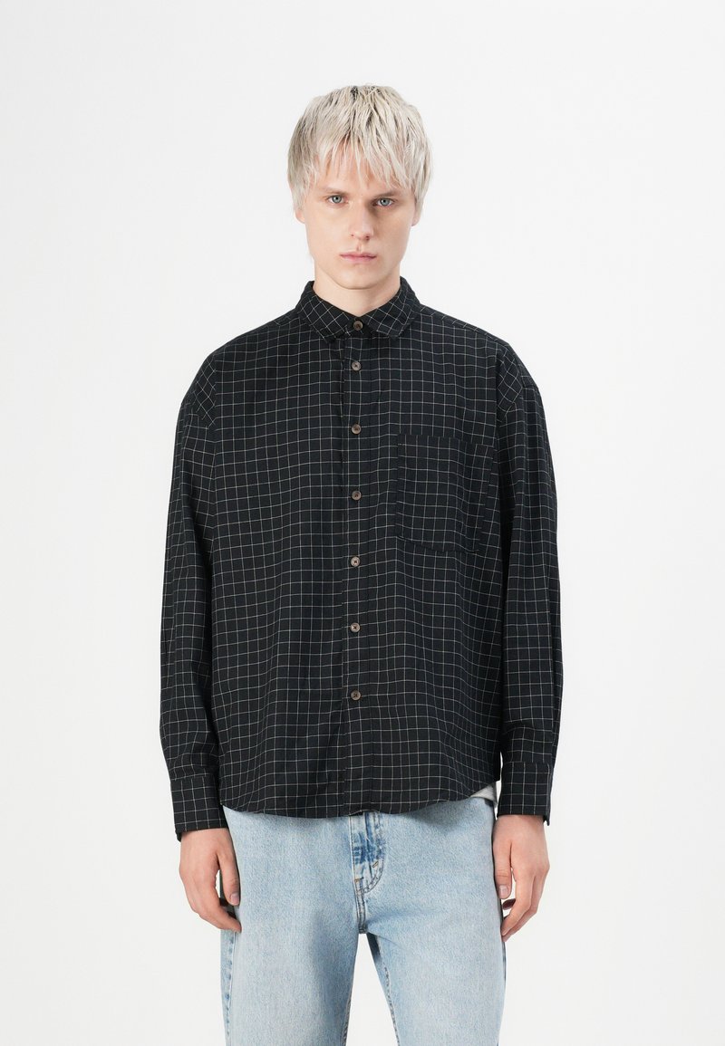 Zwarte shirt met wit ruitpatroon, met een button-down kraag, lange mouwen en borstzak. De stof lijkt soepel met een gestructureerde pasvorm.