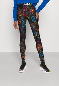 Tajta leggings gjorda av elastiskt tyg, med ett färgglatt barockmönster på en svart bakgrund, tillsammans med distinkta svarta skor.