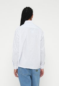 Hvit langermet skjorte med blå vertikale striper, knapp-up krage og løs passform. Kombinert med lyseblå denim bukser.