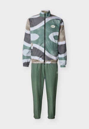 Žalia ir smėlio spalvos raštuotas užsegamas švarkelis su elastinėmis rankogaliais ir žalios spalvos kelnės su elastine juosmeniu, su EA7 logotipais ant krūtinės ir šlaunies.