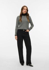 Sivi džemper s imitacijom visokog ovratnika, crne hlače širokih nogavica i crni remen. Glatka tekstura s uskim krojem i kontrastnim naglascima na manšetama.