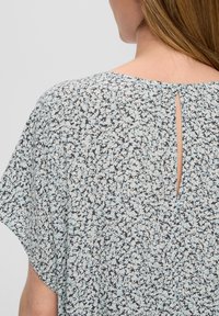 Luftige Bluse in Hellblau mit schwarzem und weißem Blumenmuster. Sie hat einen runden Ausschnitt und ein kleines Schlüsselhole-Detail im Rücken.