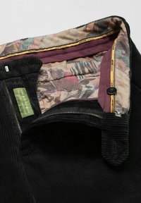 Schwarze Cordhose mit einem Futter mit Blumenmuster; verfügt über einen vorderen Reißverschluss, einen Knopfverschluss und ein grünes Stoffetikett.