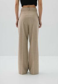 Beżowe spodnie o szerokich nogawkach z wysokim stanem, subtelny wzór w kratkę, dwie tylne kieszenie i prosty krój, wykonane z teksturowanej tkaniny.