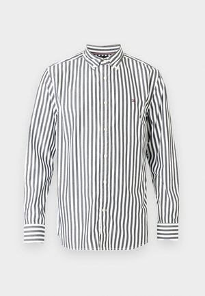 Pruhovaná košeľa v čiernej a bielej farbe s golierom na gombíky, dlhými rukávmi a malým logom na hrudi. Má kontrastné pruhované manžety.
